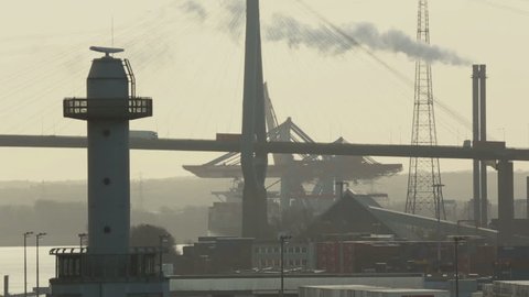 Industrial landscape silhouette - pipes with steam and trucks carrying containers on the high bridge