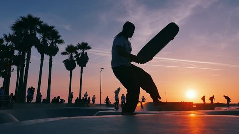 Skateboarder silhouettes skateboarding in Venice Beach skate park at sunset. Slow motion.