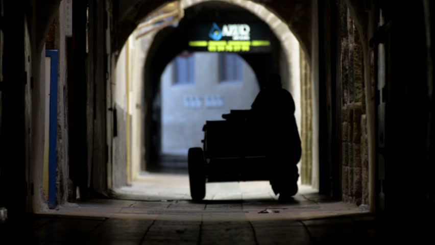 Dark old corridor of Essaouira in Morocco and the seller with a cart in national dress walking away from the camera