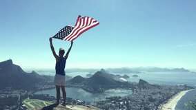 Man stands holding an American flag at a bright overlook of the city skyline of Rio de Janeiro, Brazil