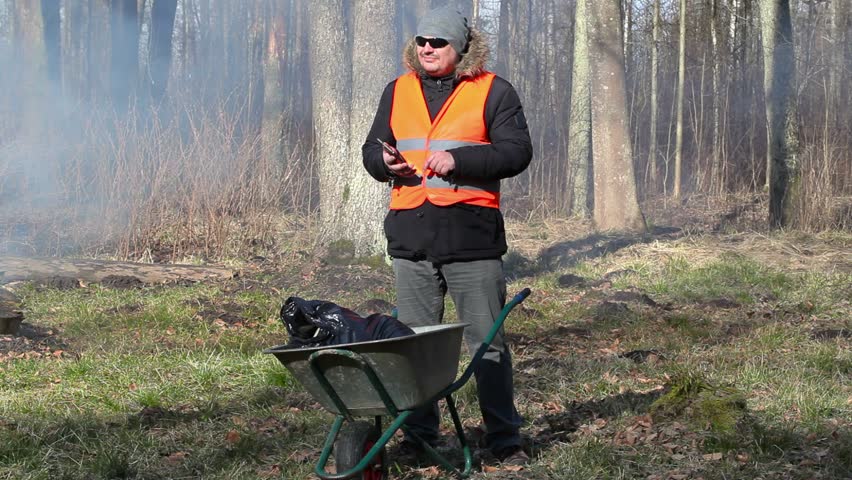 Man with smart phone and wheelbarrow near the bonfire