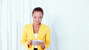 Smiling female model with tablet. The video of modest business woman on white background in a yellow jacket