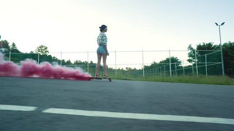 Young fashion girl riding wooden skateboard with red smoke on the city road