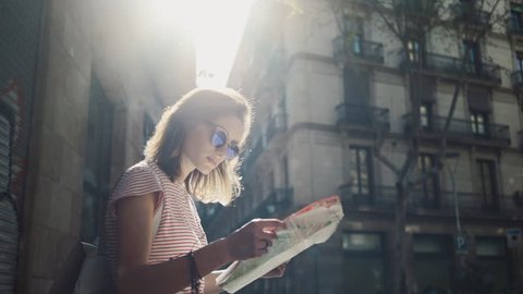 Young tourist woman exploring Barcelona map while traveling in Spain, vacation concept, flare light