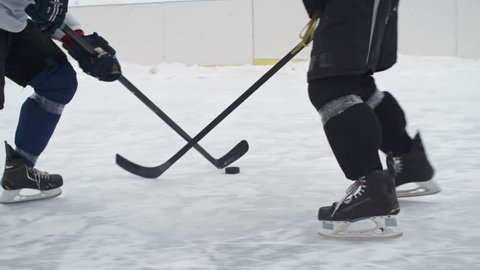 Tracking shot of a hockey forward carrying a puck while being pressured by an opposing defenseman and taking a slap shot being blocked by goalie