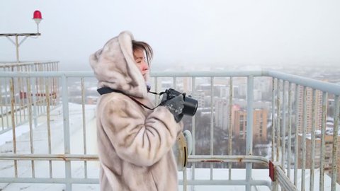 Woman in fur coat directing camera and photographing on roof in winter.