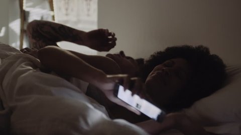 Mixed Race Couple waking up in bed looking at alarm on smart phone