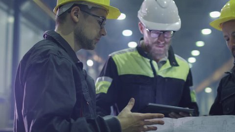 Team of workers at a heavy industry factory have a conversation while looking at a blueprint. Shot on RED Cinema Camera.