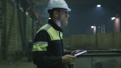 Engineer in hardhat is moving through a heavy industry factory with a tablet computer. Shot on RED Cinema Camera.