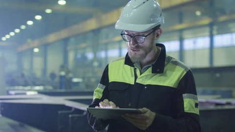Engineer in hardhat is using a tablet computer in a heavy industry factory. Shot on RED Cinema Camera.