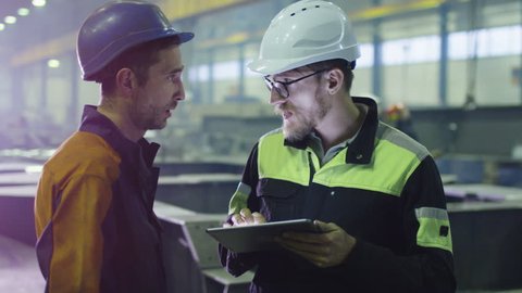 Engineer and worker in hardhats are having a conversation in a heavy industry factory. Shot on RED Cinema Camera.