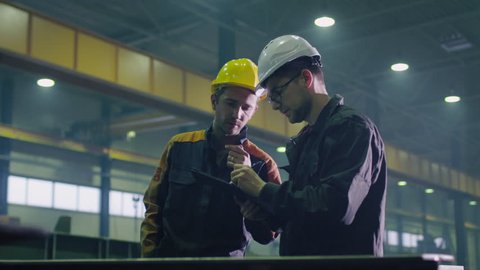 Manager and engineer worker in hardhats are having a conversation in a heavy industry factory. Shot on RED Cinema Camera.
