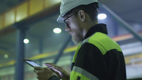Engineer in hardhat is holding a tablet computer in a heavy industry factory. Shot on RED Cinema Camera.