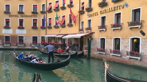 VENICE ITALY 04 OCT 2015: gondolas and gondoliers at canal, hotel in background. Travel to Europe, venetian city at water. Romantic italian tourism, old architecture landmarks, cityscape. Tourist boat Redaktionell stockvideo