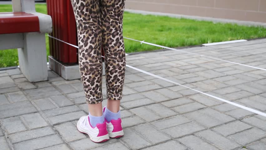Girl jumping over band hooking and releasing it next to bench on street.