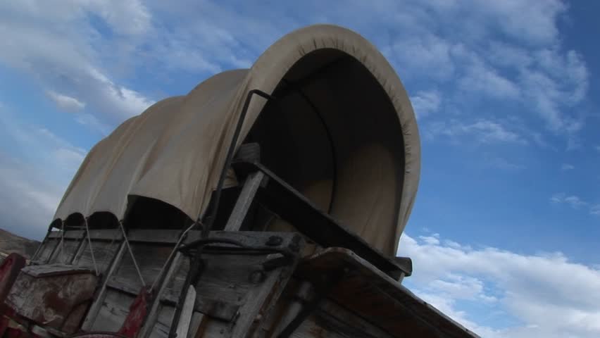 Low angle of a covered wagon against a blue sky.