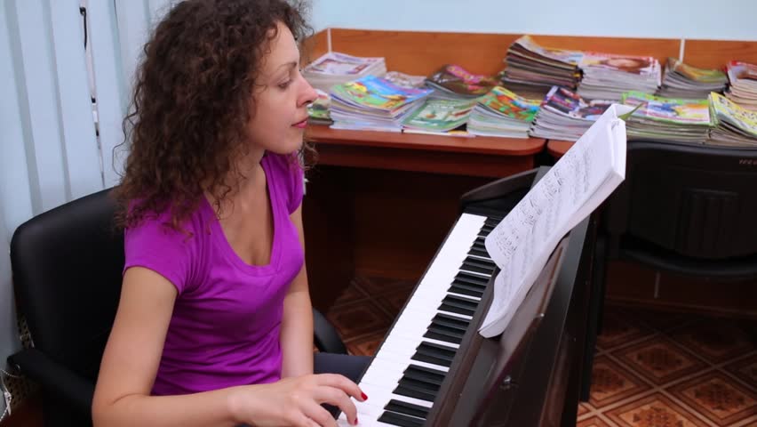 Brunette woman playing electronic piano and looking at notes.