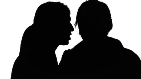A woman whispering a secret in the ear of a man. Silhouette shot.
