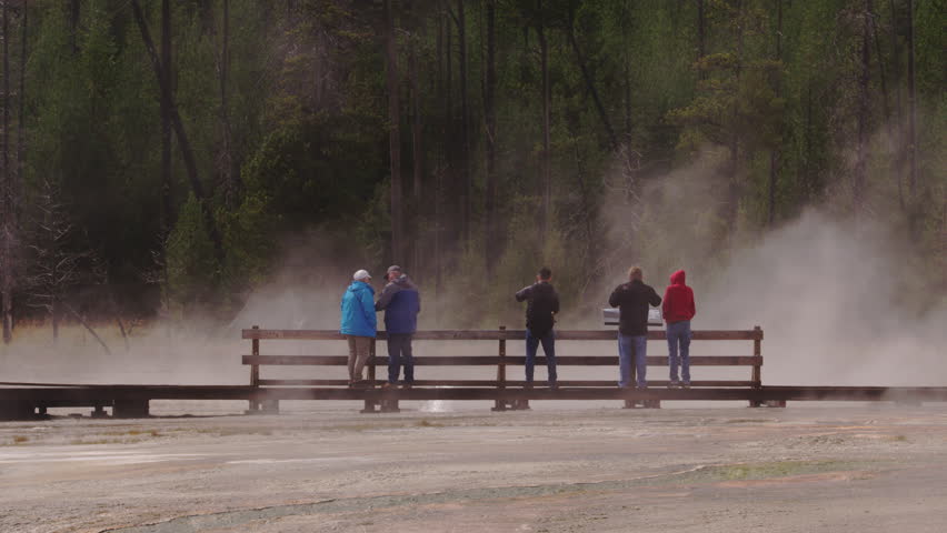 People standing on boardwalk looking at steaming hot springs in Yellowstone National Park, Wyoming and Montana, USA. 4K.