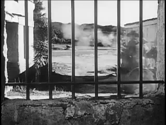 Point of view through prison bars of cowboys on horseback during shootout, 1940s