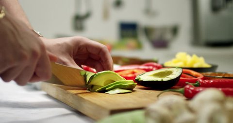 Slicing avocado in a kitchen environment. Cutting fresh vegetables on a wooden bench in a modern kitchen with shallow focus and blurred background. Strong and vivid colors.