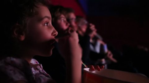 Little girl watching a movie and eating popcorn at the movie theater