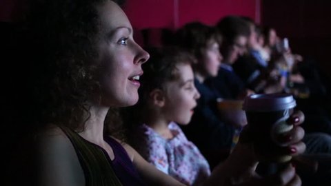 A woman watching a movie in a theater with children and friends and smiling