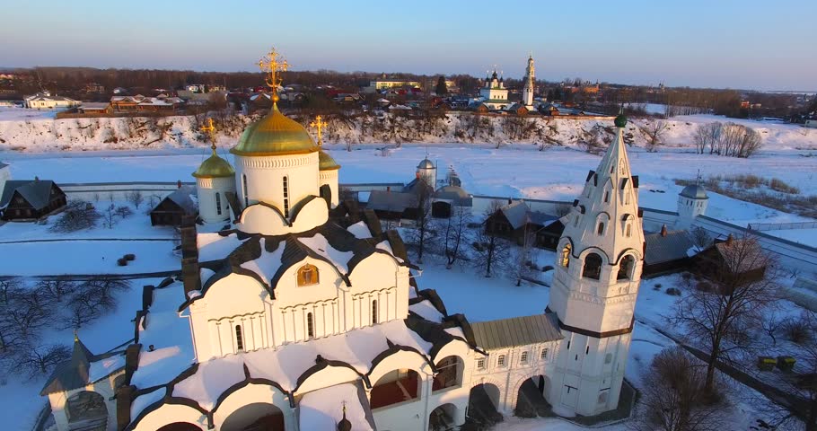 Spinning around the Pokrovsky Cathedral (1510-18) and belfry (17 century) at the Pokrovsky monastery (1364) in a crook of the Kamenka River, in old russian town Suzdal. Aerial. Winter sunset		