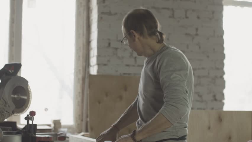Aged carpenter in glasses checking wooden board after polishing. Manufacturer. Furniture. Treatment