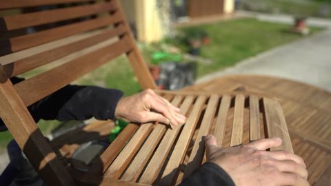 Personal perspective of  carpenter's hand restoring a wooden chair with sandpaper. Garden furniture. POV.