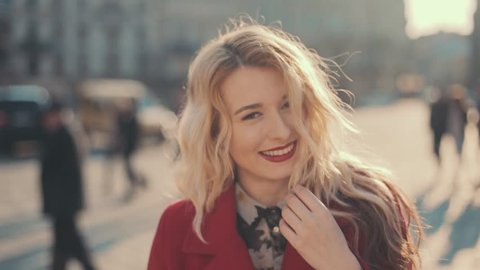 Attractive young woman with red lips in the city turning to camera and smiles, steady cam shot, slow motion Video Stok