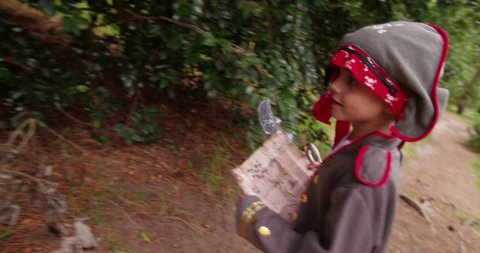 Boy dressed up as little pirate is excited to find the gold coins in treasure chest and is hunting through park after treasure with his map.