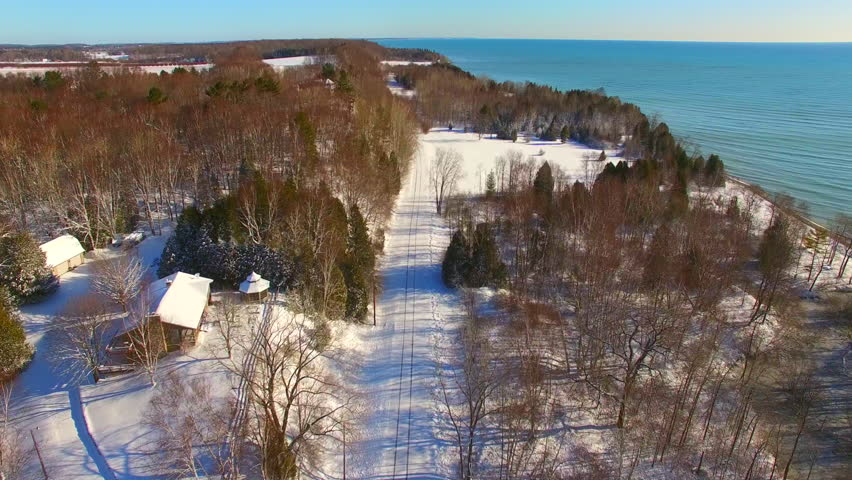 Snowy scenic road along Lake Michigan shoreline, Door County Wisconsin, aerial flyover.
