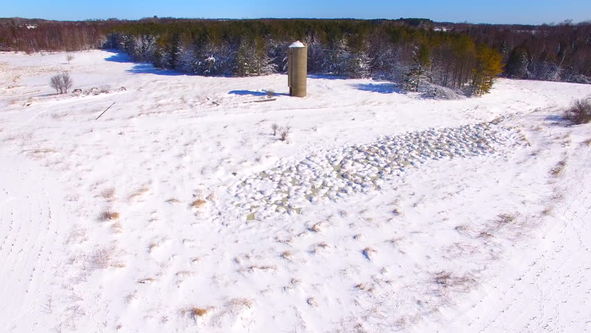 Scenic aerial flyover of snow covered woods and fields with abandoned silo, rural Wisconsin.