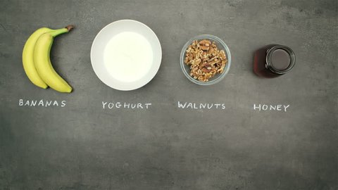 Banana dessert with yogurt, walnuts and honey. Top view on ingredients and preparation on grey kitchen table. Stop motion animation and timelapse eating.