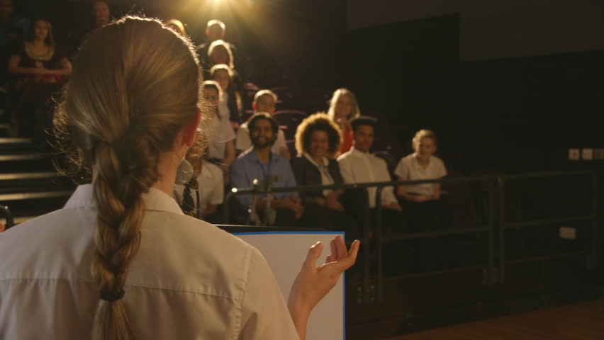 Over the shoulder view of a teenage girl giving a presentation to a group of students and teachers in her school. Royalty-Free Stock Footage #15582952