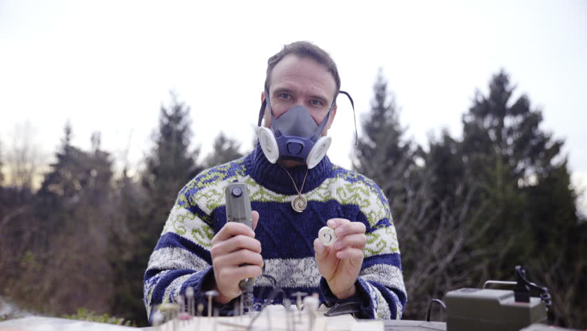 Person with pendant and hand drill posing 4K. Sliding from right to left over table with man looking in camera and holding in each hand a finished pendant and electric drill in another.