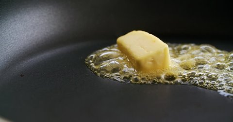 Cube of butter melting sizzling browning in non stick pan skillet in slow motion, preparation for cooking