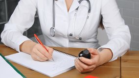 Beautiful young female doctor sitting in front of working table holding jar of tablets and writing prescription on special form. Medical and pharmacist concept