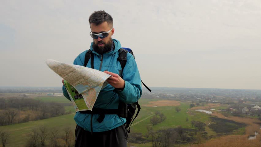 Man tourist in a blue jacket with a backpack looking on the map