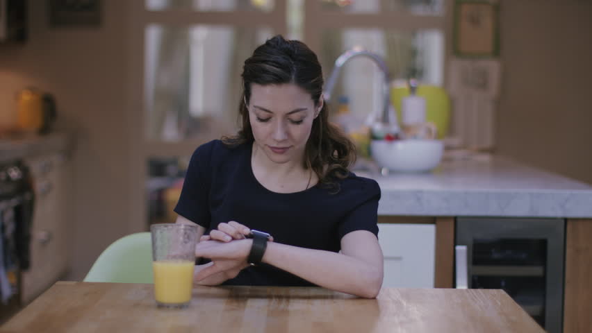 Young adult woman using smart watch at home on kitchen table