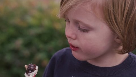 Little girl eating a cake pop outside, close up