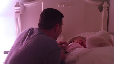 A father tucks his daughter into bed and gives her a goodnight kiss
