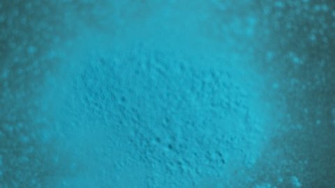 Blue holi powder bounces off black canvas background in shockwave pattern, slow motion closeup Stockvideó