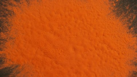 Orange holi powder bounces off black canvas background in shockwave pattern, slow motion closeup Stockvideó