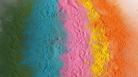 Colorful rainbow holi powder bounces off white canvas background in shockwave pattern of green blue pink and orange, slow motion, closeup