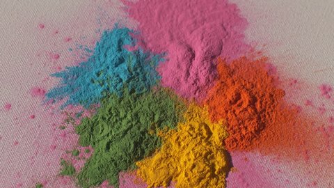 Colorful rainbow holi powder bounces off white canvas background in rainbow shockwave pattern, slow motion