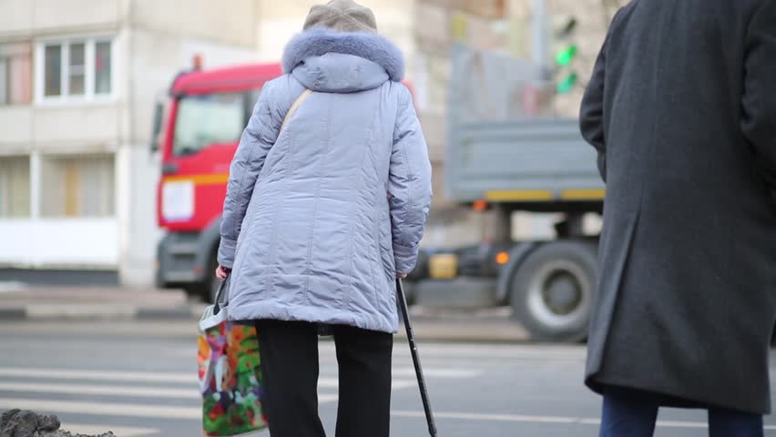 Elderly people man and woman stand at sidewalk waiting for green signal of traffic light.