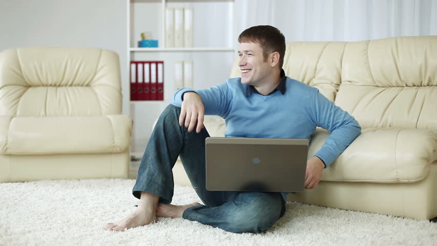 Smiling young man with laptop on carpet 