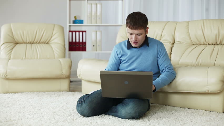 Young man looking at camera with laptop on carpet 